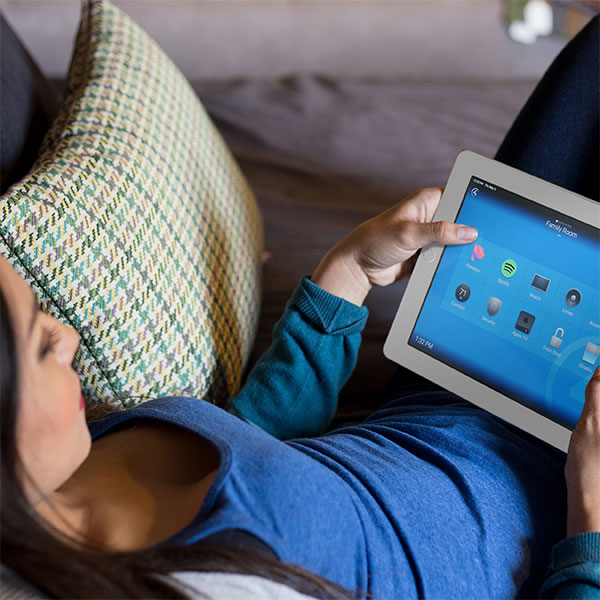 Woman lies on her sofa with an iPad displaying the Control4 Smart home display.